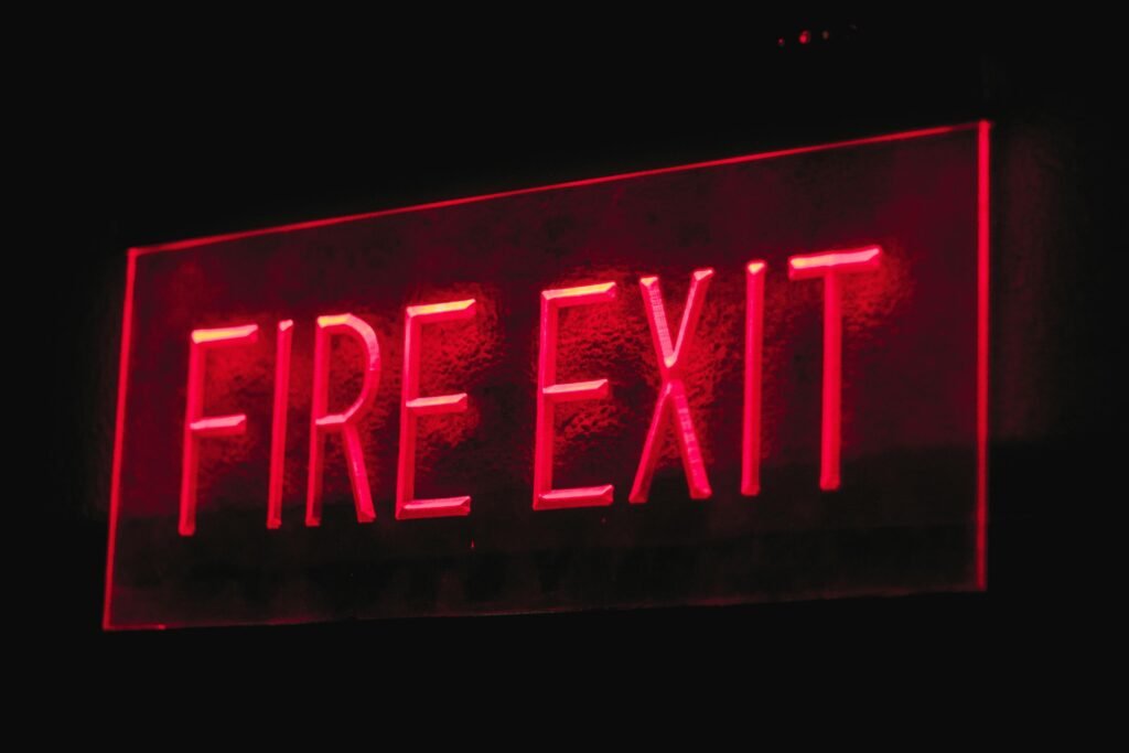 Brightly lit red neon fire exit sign illuminating in a dark setting.